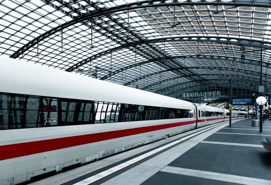 Inside Hackney Central station, the image showcases a modern, high-speed train with a sleek white exterior and a red stripe along the side, positioned on a clean, well-maintained platform. The station features an expansive glass and steel arched roof allowing natural light to illuminate the area. The platform's surface appears smooth and free of dust or debris, with visible markings and signs guiding passengers. Nearby, a clock displays the current time, and there are minor elements like benches and waste bins visible. The overall scene highlights the station's hygienic and orderly condition, emphasizing the importance of surface cleaning and maintenance for public spaces. Carpet Cleaners E5 is committed to delivering professional sanitisation and deep cleaning solutions for commercial environments such as train stations, ensuring hygiene and safety for commuters.